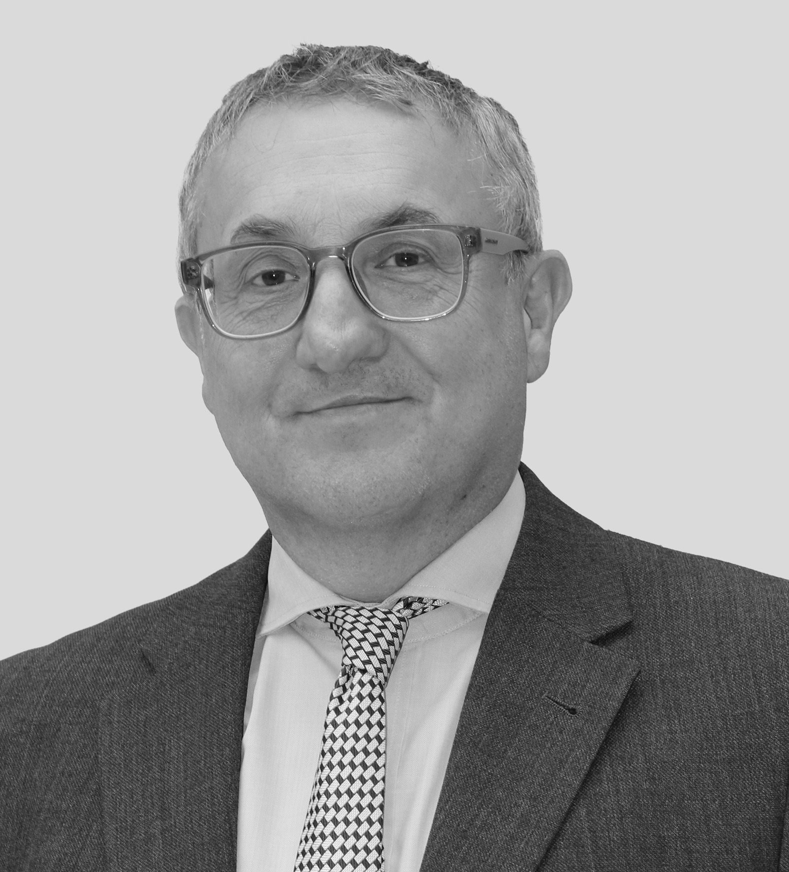 Studio headshot of man in glasses, suit and tie against grey backdrop