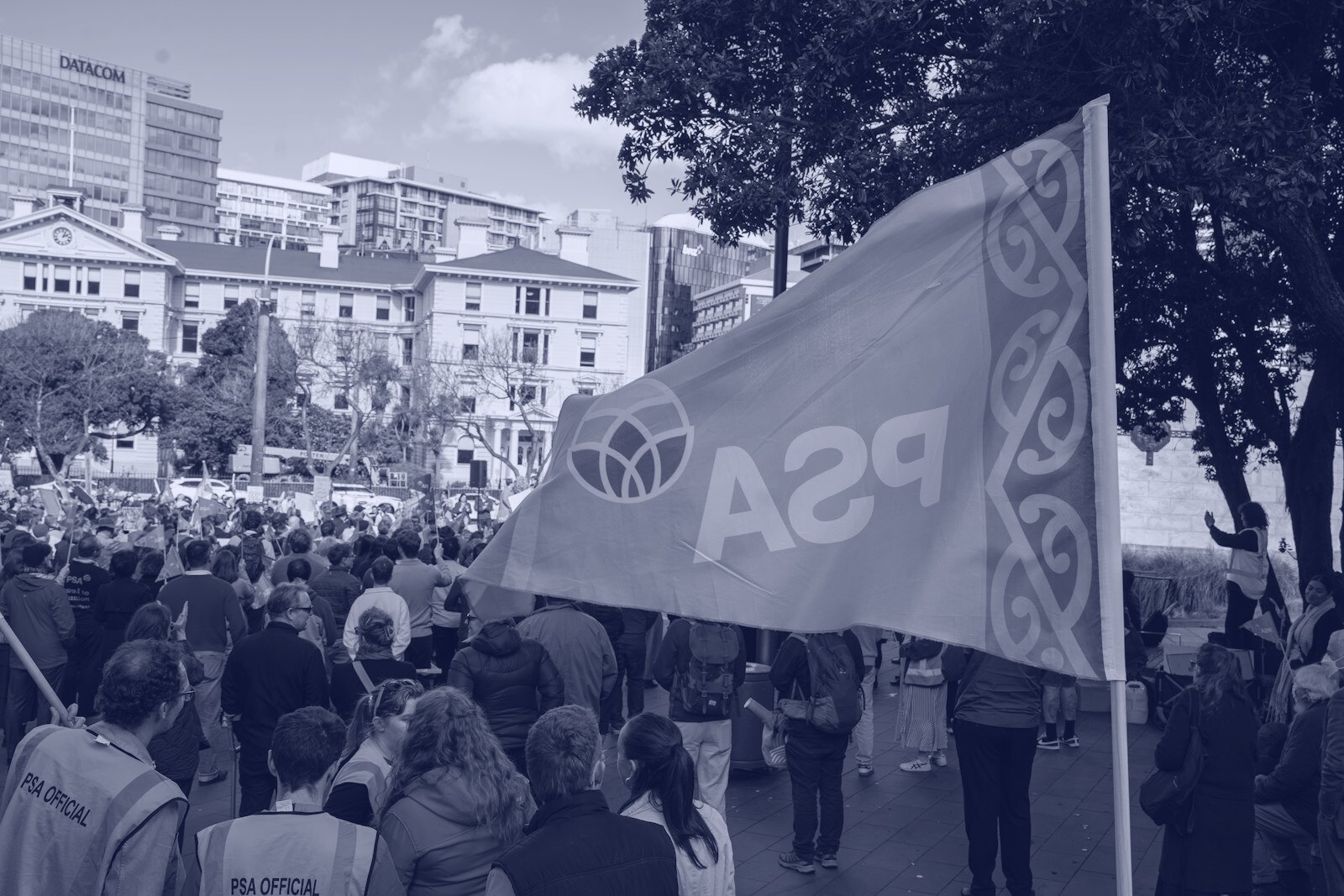 An orange flag with a logo and text waving above a crowd of people